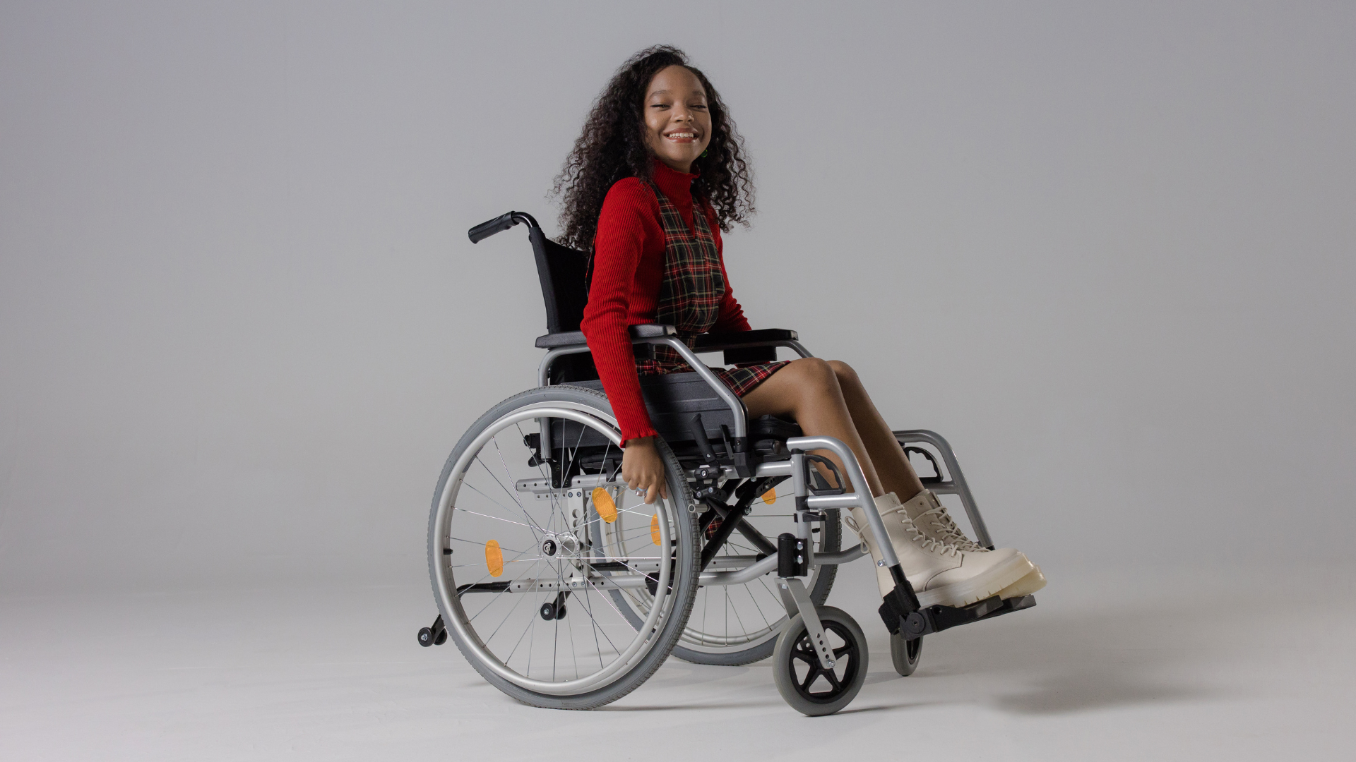 spina bifida child on wheelchair is wearing red sweater and smiling